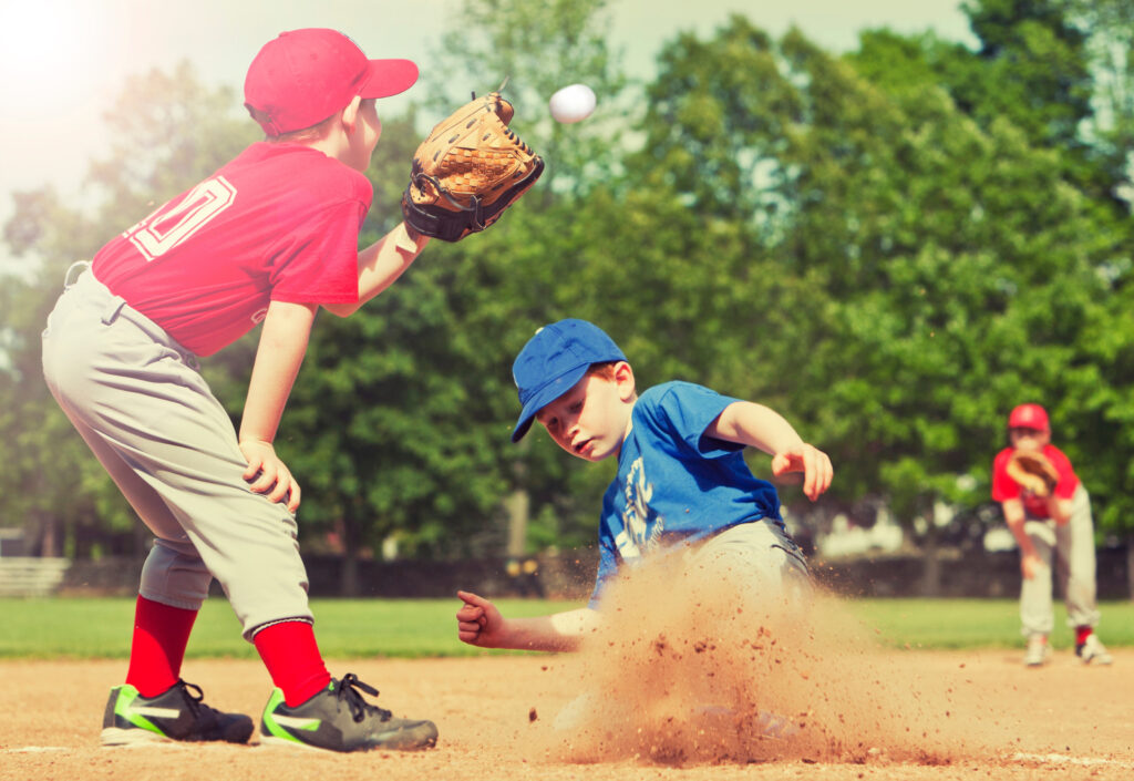 Young baseball player sliding into home plate as another reaches for the ball, symbolizing faith and teamwork.